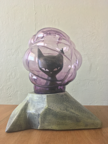 sculpture of a black kitty sitting on an angular rock and inside of a bulbous purple-tinted glass pod