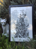 the same framed drawing leaned against a lavender bush and next to a white ceramic cat with green eyes and a chipped ear