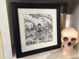shows the drawing in a sweet black vintage frame with white matting sitting on a white box shelf next to a skull with red gem eyes.