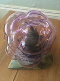 top-down view from the back, off-center angle. the rock peeks out from under the glass on the left and on the right are and tail stick out from the silhouette of the cat above the wooden table. the purple-tinted glass is very warped and bulbous like a thought bubble or a magical cloud